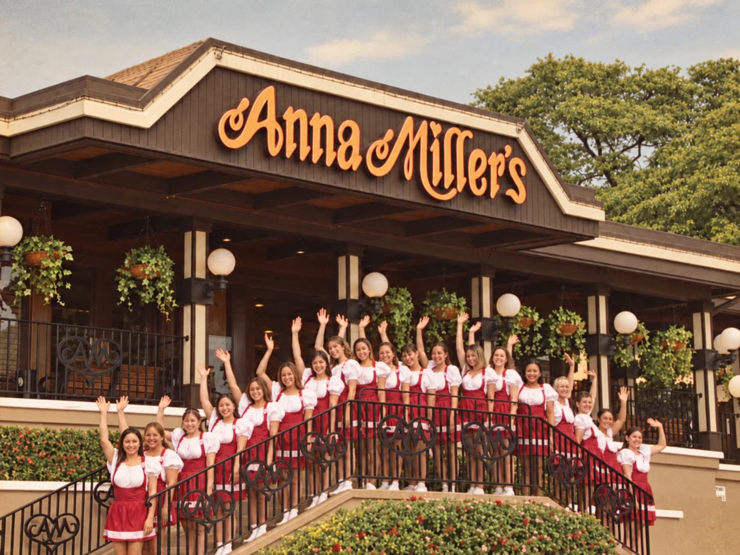Anna Miller’s staff waving from the restaurant steps beneath the original sign